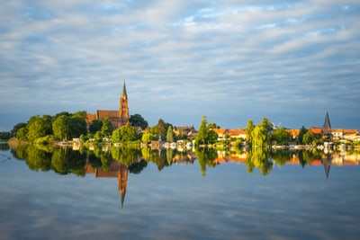 Stadtlandschaft am See mit Kirche und Wolkenhimmel.