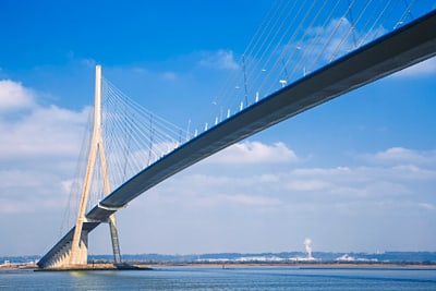 Schrägseilbrücke über ruhiges Gewässer unter blauem Himmel.