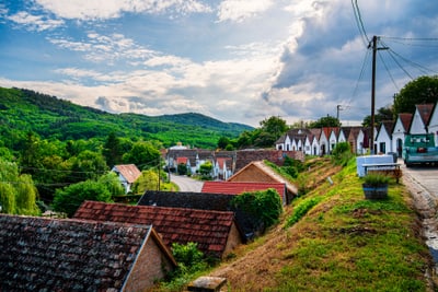 Landschaft mit Hügeln, kleinen Häusern und bewölktem Himmel.