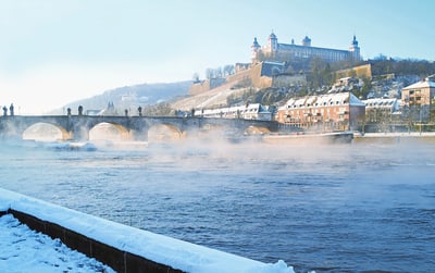adventsflusszauber-main-7.jpg Alte Brücke und Festung am Fluss in winterlicher Landschaft.