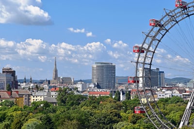 Stadtpanorama mit Riesenrad, Gebäuden und Bäumen im Vordergrund.