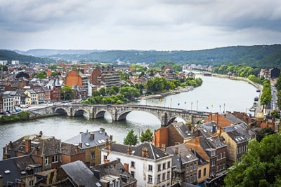 Stadtlandschaft mit Fluss und Brücke, umgeben von Gebäuden und grünen Hügeln.