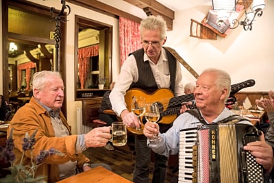 Musiker mit Bier und Akkordeon stösst mit Gästen im Restaurant an.