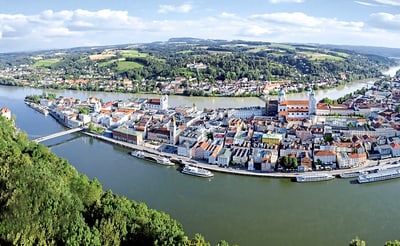 Luftaufnahme einer Stadt an einem Fluss mit Brücken und Booten, umgeben von Hügeln.