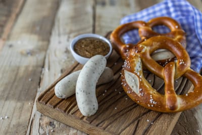 Holzbrett mit Brezeln, Weisswürsten und Schüssel mit Senf.