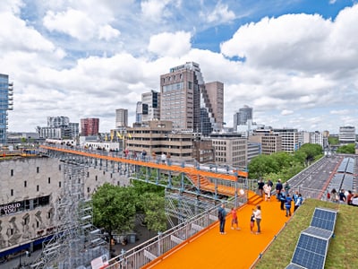 Stadtansicht mit erhöhtem, orangefarbenem Weg und Menschen.