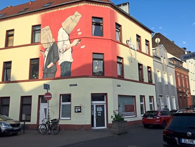 Eckgebäude mit Wandgemälde zweier Figuren mit Papiertüten auf dem Kopf.