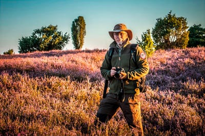 Person mit Hut und Kamera auf einem Feld mit blühenden Pflanzen.