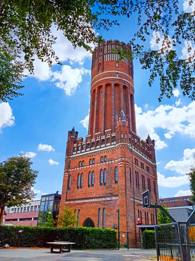 Historischer Wasserturm aus rotem Backstein vor blauem Himmel.