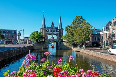 Blumen vor einem Kanal mit mittelalterlichem Stadttor und Boot.