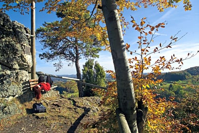 Person auf einer Bank mit herbstlicher Landschaft im Hintergrund.