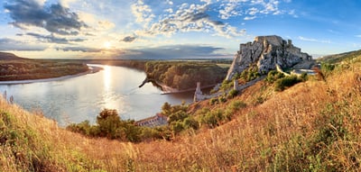 Burgruine an einem Flussufer bei Sonnenuntergang.