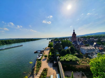 Landschaft mit Fluss, Kirche und Dorf im Sonnenlicht.