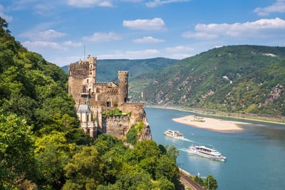 Burg am Rhein mit Fluss, Hügeln und Schiffen.