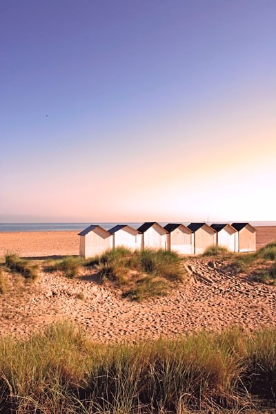 Strandhütten am Meer mit Sand und Dünen im Vordergrund.