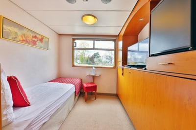 Kleines Gästezimmer mit Einzelbett, Fenster und Fernseher.
