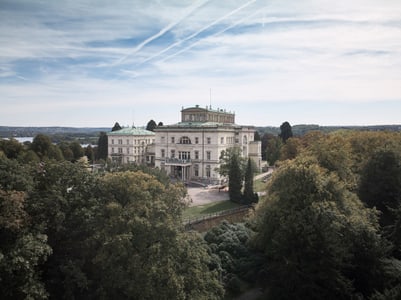 Historisches Gebäude umgeben von Bäumen mit Blick auf den See im Hintergrund.