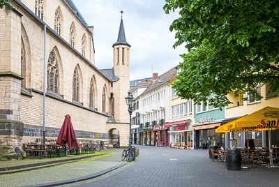 Stadtstrasse mit alten Gebäuden, Sitzgelegenheiten im Freien und Sonnenschirmen.