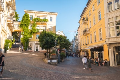 Eine gepflasterte Strasse mit alten Gebäuden, Bäumen und Menschen, die herumlaufen.