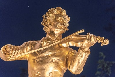 Goldene Statue eines Violinisten im Freien bei Nacht.