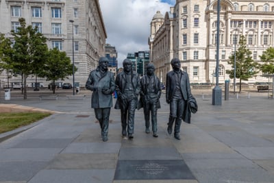 Denkmal von vier gehenden Personen in einer städtischen Umgebung mit historischen Gebäuden.