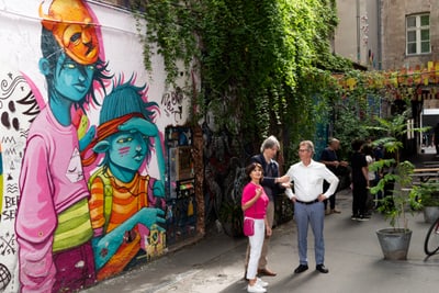 Strassenszene mit bunter Graffiti-Wand und vier Menschen, die stehen und gehen.