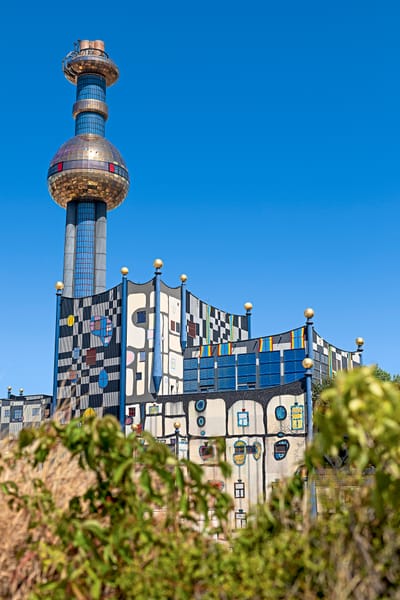 Buntes Gebäude mit Turmspitze und bewachsener Vordergrund.