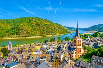 Malerische Stadt am Fluss mit Kirche und grünen Hügeln im Hintergrund.