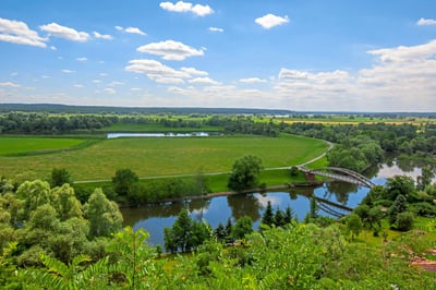 Landschaft mit Fluss, Brücke und grünen Feldern.