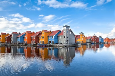 Bunte Häuser spiegeln sich in ruhigem Wasser unter blauem Himmel.