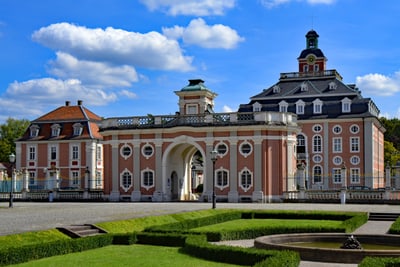 Barockschloss mit prachtvollen Gärten und blauem Himmel.