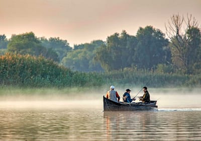 Drei Personen in einem Ruderboot auf nebligem See.