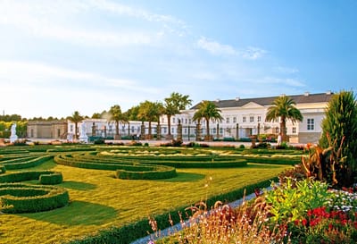 Barockgarten vor einem grossen, weissen Gebäude bei Sonnenschein.