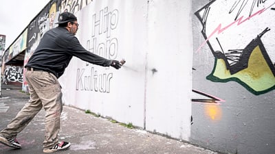 Mann sprüht Graffiti auf eine Wand mit Schriftzug 'Hip Hop Kultur'.