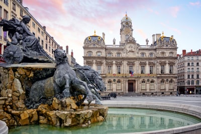 Historisches Gebäude mit Brunnen und Skulpturen im Vordergrund.