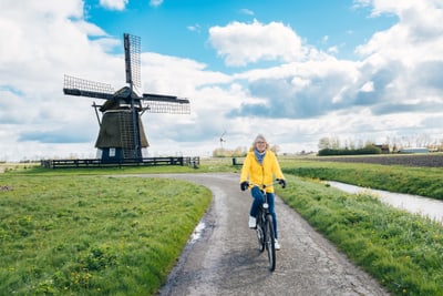 Frau fährt auf einem Landweg Fahrrad, Windmühle im Hintergrund.