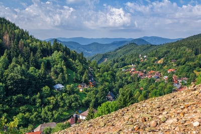 Blick auf ein grünes Tal mit Wald und Dorf, umgeben von Bergen.