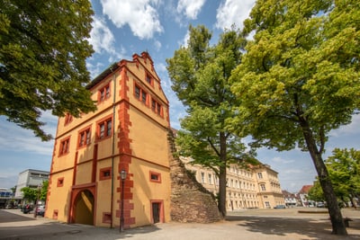 Altes Gebäude mit roter Verzierung neben Bäumen unter blauem Himmel.