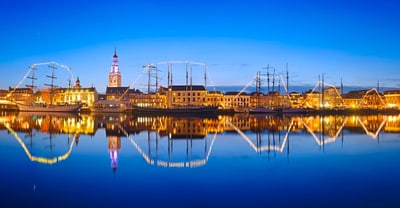Beleuchtete Schiffe und Gebäude bei Nacht, spiegeln sich im Wasser.
