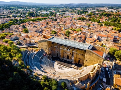 Luftaufnahme eines antiken Theaters in einer Stadt mit roten Dächern und grüner Landschaft im Hintergrund.