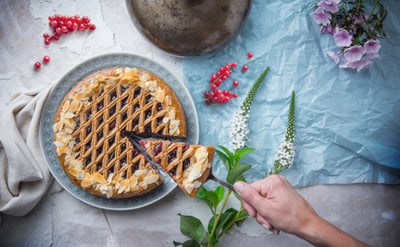 Eine Hand nimmt ein Stück Kuchen von einem Teller, umgeben von Blumen und Beeren.
