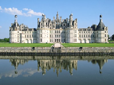 Historisches Schloss mit Türmen und Wassergraben im Vordergrund.