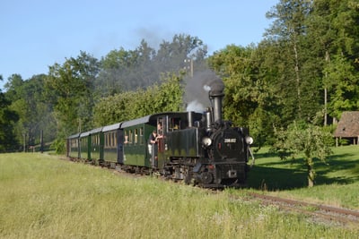 Dampflok auf ländlicher Strecke mit Passagieren.