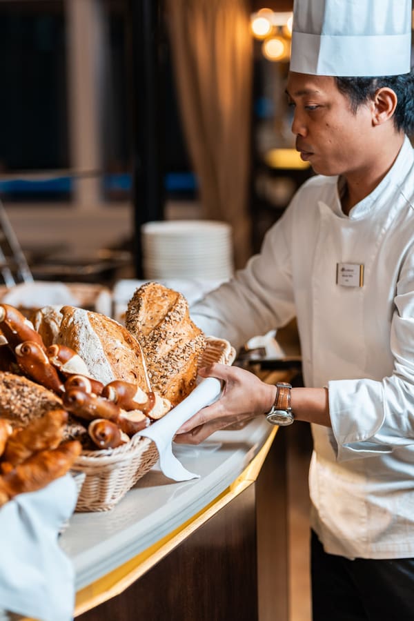 Koch in weisser Uniform richtet Brot- und Gebäckkorb an.